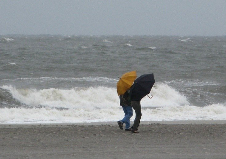 Duas pessoas de guarda-chuva andando na areia da praia